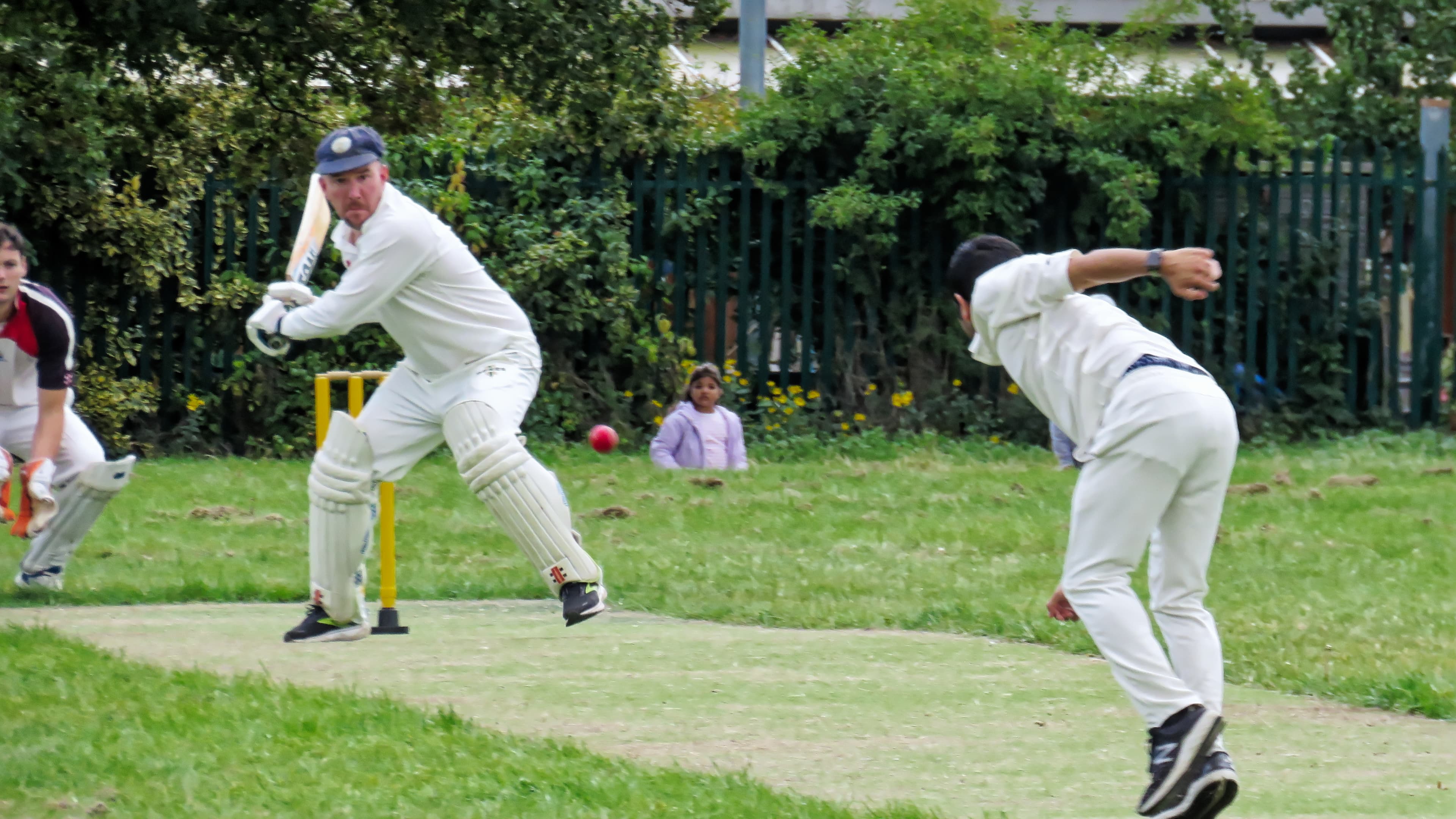 Partido de críquet con bateador, wicketkeeper, stumps y fielders visibles